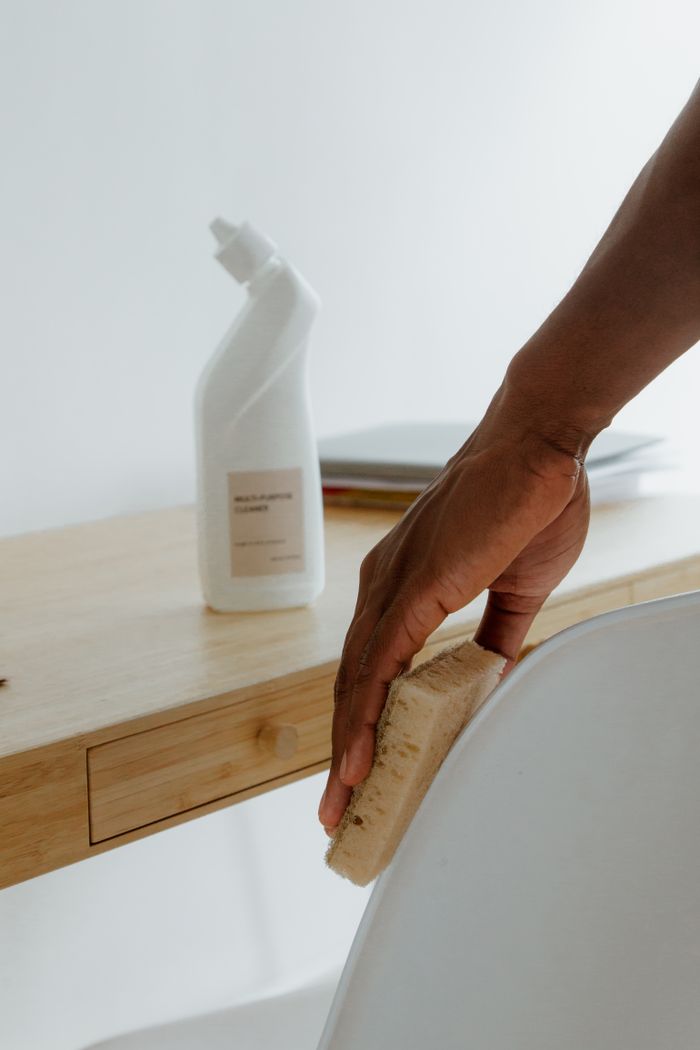 Minimalist room with a person cleaning a chair using a sponge and cleaning product.